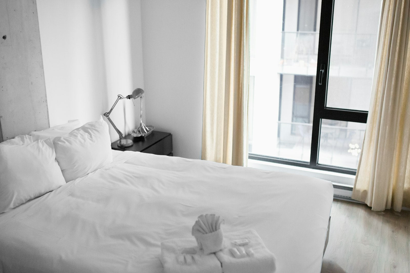 Freshly made white hotel bed beside a bright window