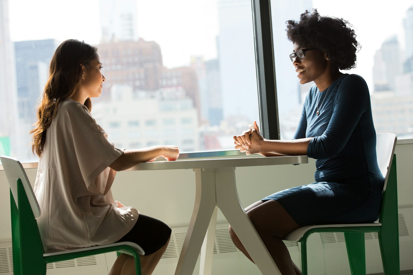 Two women in conversation across a table during a workplace meeting