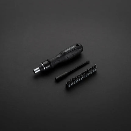 GearX ratchet screwdriver lying on a workbench with various screwdriver bits and tools nearby.